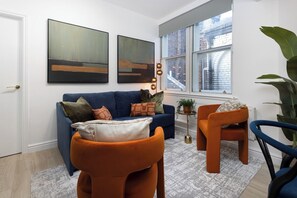 A modern living room with a blue sofa, orange armchair, and a small side table with a plant. - Flatzy City Centre Retreat  Sleeps 8  2 baths (Liverpool)