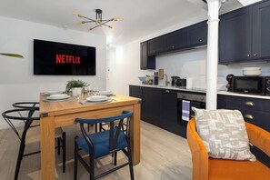 Eine moderne Küche mit dunklen Schränken, einem Holztisch und einem darüber montierten Fernseher, der 'NETFLIX' anzeigt.