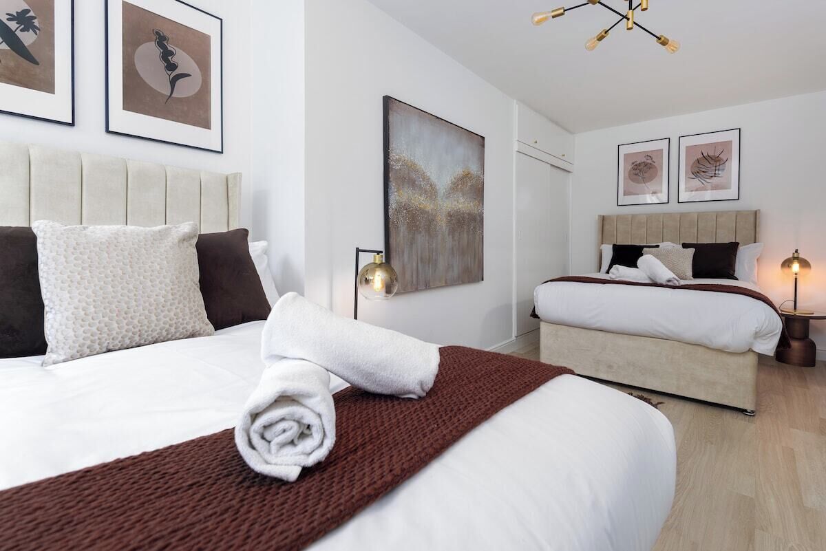 Quarto de hotel com duas camas, uma grande obra de arte na parede e um lustre moderno.