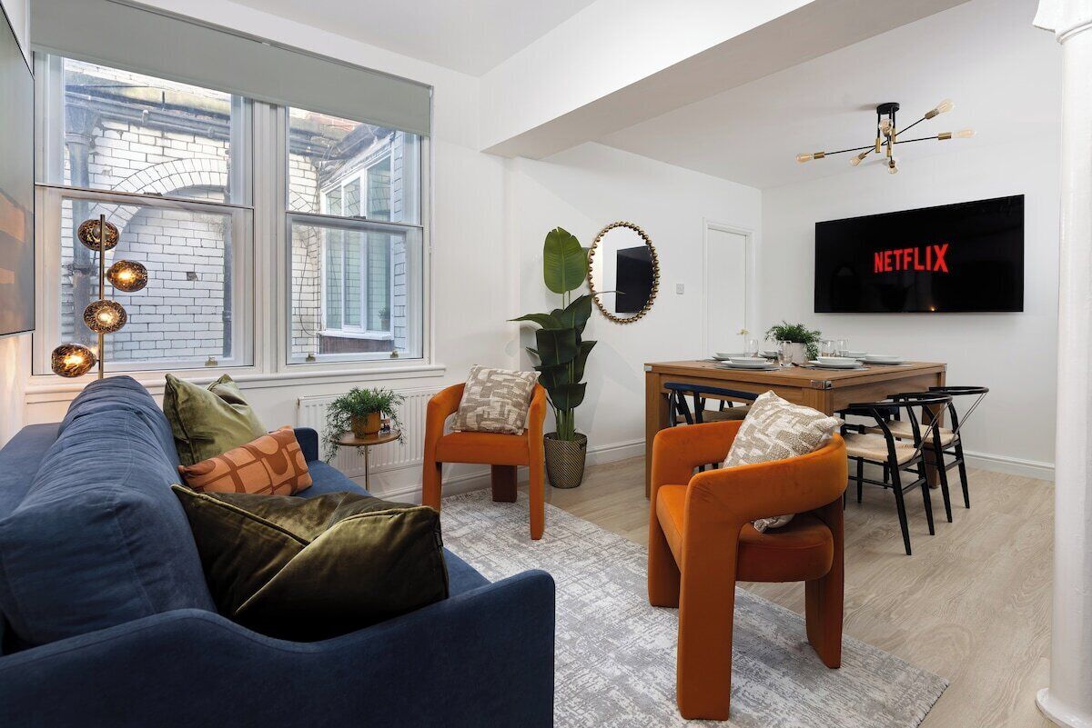 Een moderne woonkamer met een bank, stoelen, een eettafel en een televisie aan de muur.