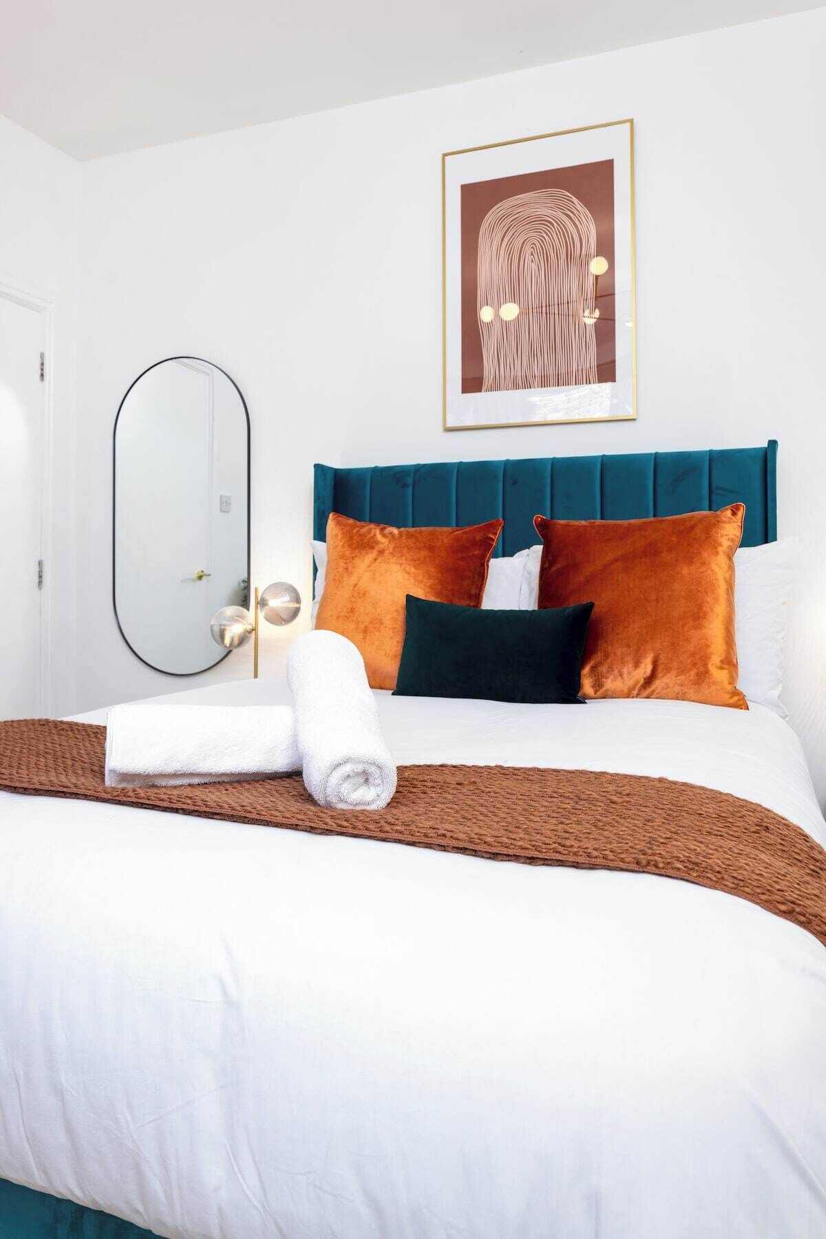 Ein Hotelzimmer mit einem Bett, einem großen Spiegel, einem gerahmten Kunstwerk und einer Tür.