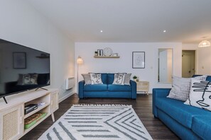 Ein modernes Wohnzimmer mit Flachbildfernseher, blauen Sofas, einem gemusterten Teppich und einer Wanduhr.