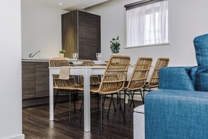 Ein moderner Essbereich mit einem weißen Tisch, Korbstühlen, einem blauen Sofa und einem Fenster mit transparenten Vorhängen.