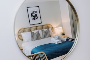 A bedroom with a bed, pillows, a bedside lamp, a framed picture on the wall, and a mirror reflecting part of the room. - Flatzy - City Centre | 2 Bathrooms | Free Parking (Liverpool)