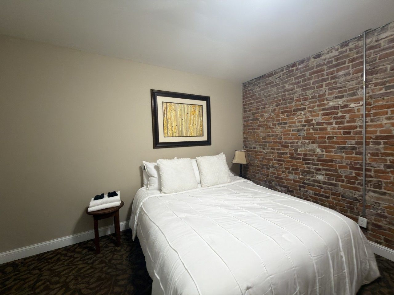Una habitación de hotel con una cama, una mesita, una lámpara y un muro de ladrillo.