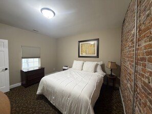 Ein Schlafzimmer mit Bett, Kommode, Lampe und einer Ziegelwand.