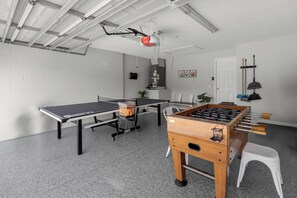 Een kamer met een tafelvoetbal tafel, een pingpong tafel en een kleine kitchenette.