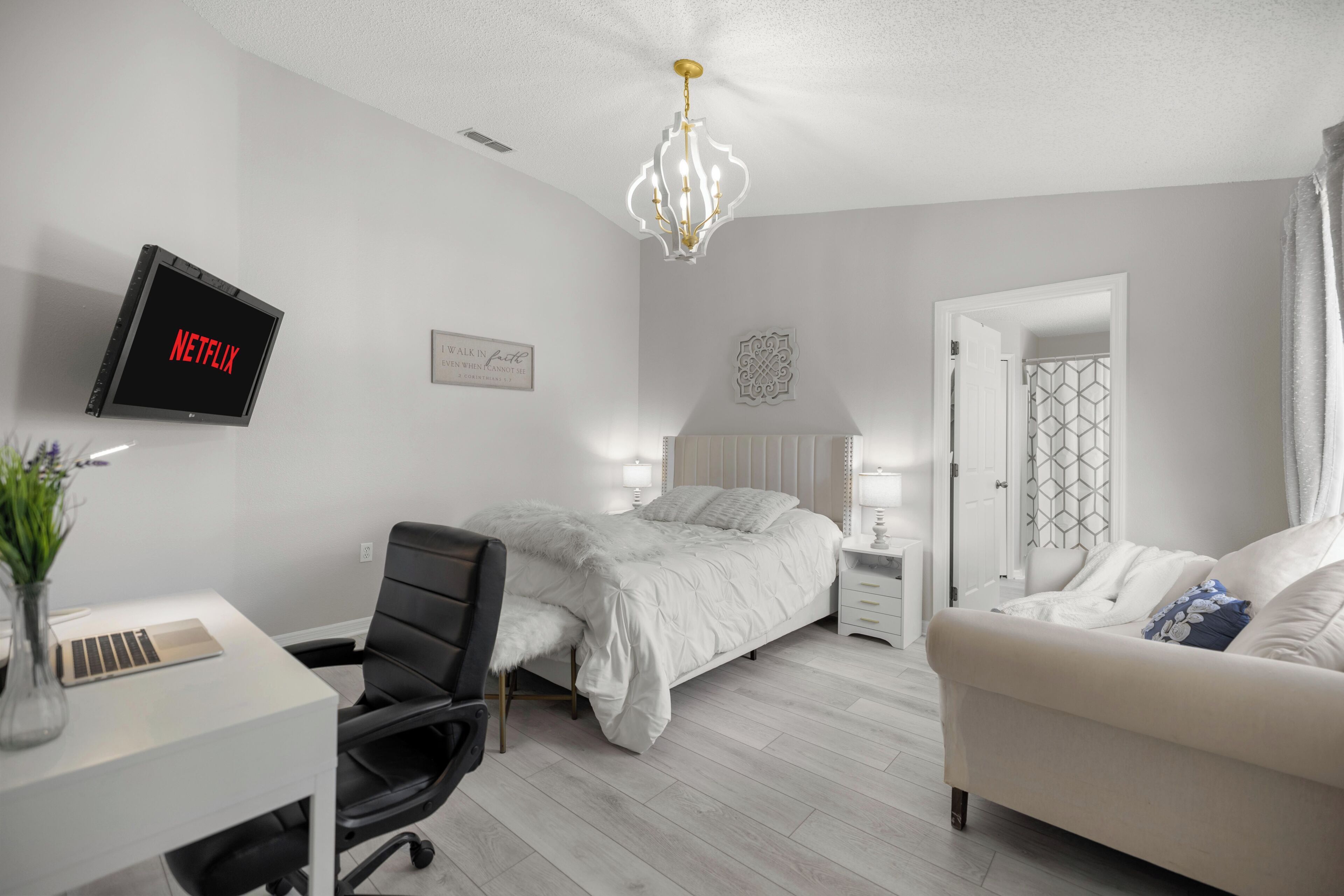 Un dormitorio moderno con una cama, un escritorio, una silla, un televisor mostrando 'NETFLIX', un adorno en la pared y una puerta con un diseño geométrico.