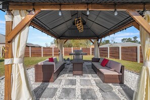 An outdoor patio with wicker furniture, a barbecue grill, and a pergola with hanging lights. - Cozy 3-bedroom house in perfect Ocala with AC for relaxing stays (Ocala)