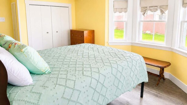 A bedroom with a bed, a nightstand, a window with curtains, and a door.