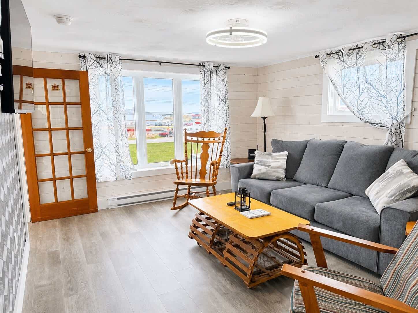 A modern living room with a grey sofa, wooden rocking chair, and a small wooden table.