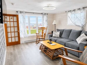 Ein modernes Wohnzimmer mit grauem Sofa, einem Holzschaukelstuhl und einem kleinen Holztisch.