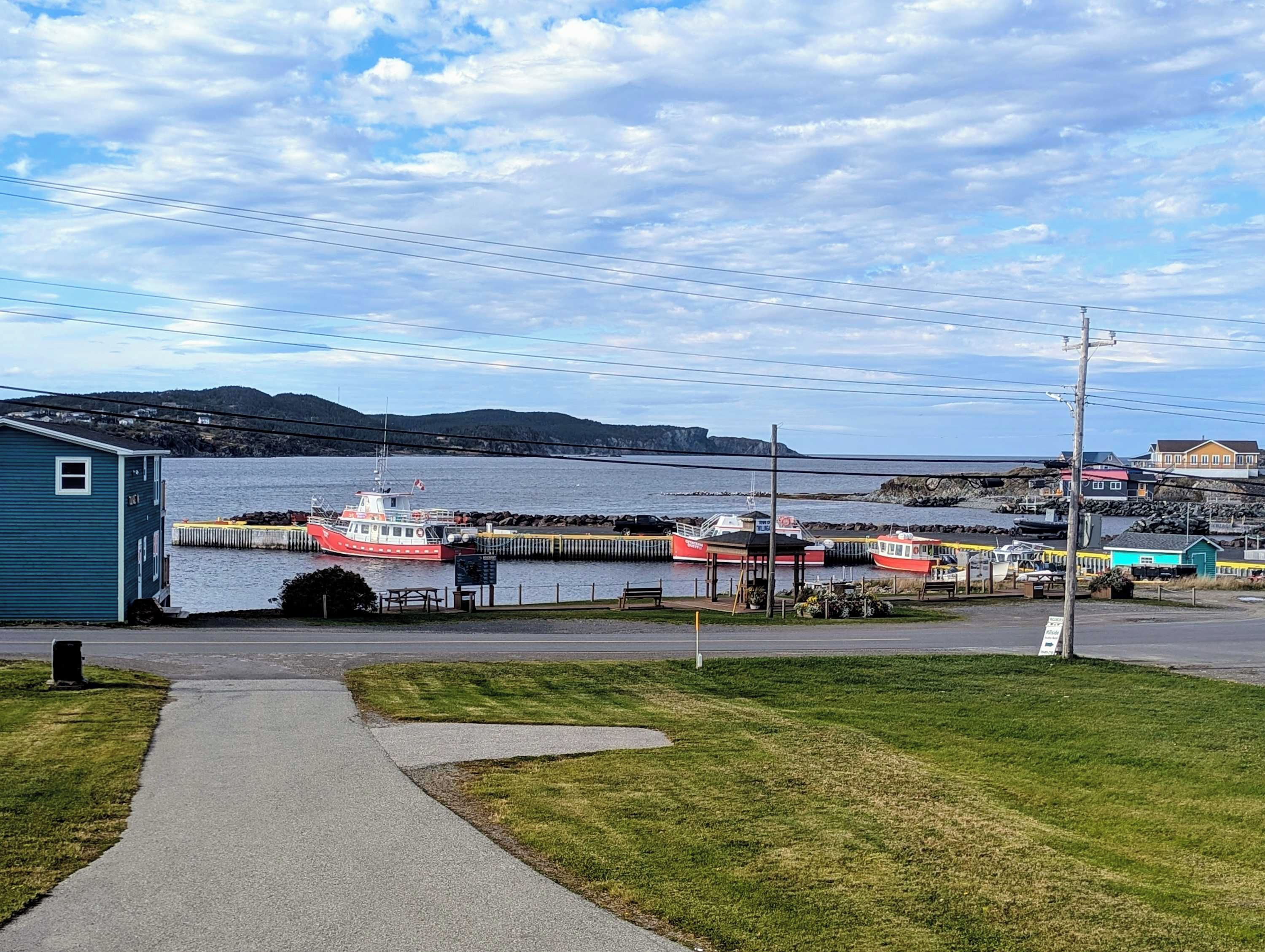 Une zone côtière avec un quai, des bateaux, un petit bâtiment et un ciel dégagé.