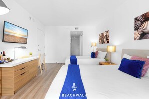 A hotel room with a bed, bedside tables, a desk, a chair, a TV, and artwork on the walls. - Beachwalk Resort Studio • Pool & Gym Access (Hallandale Beach)