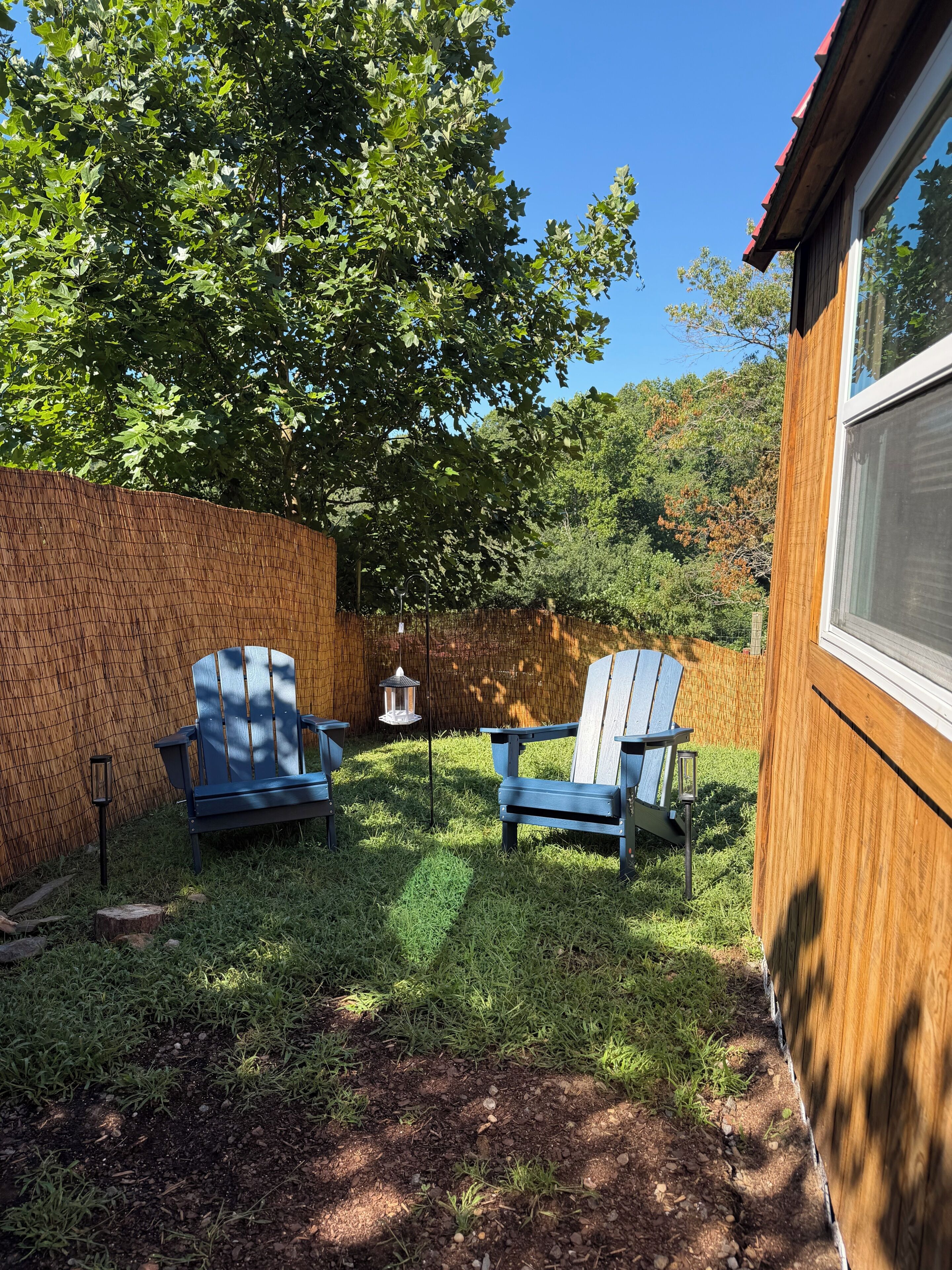 Un jardin avec deux fauteuils Adirondack, une clôture en bois et une maison avec une fenêtre.