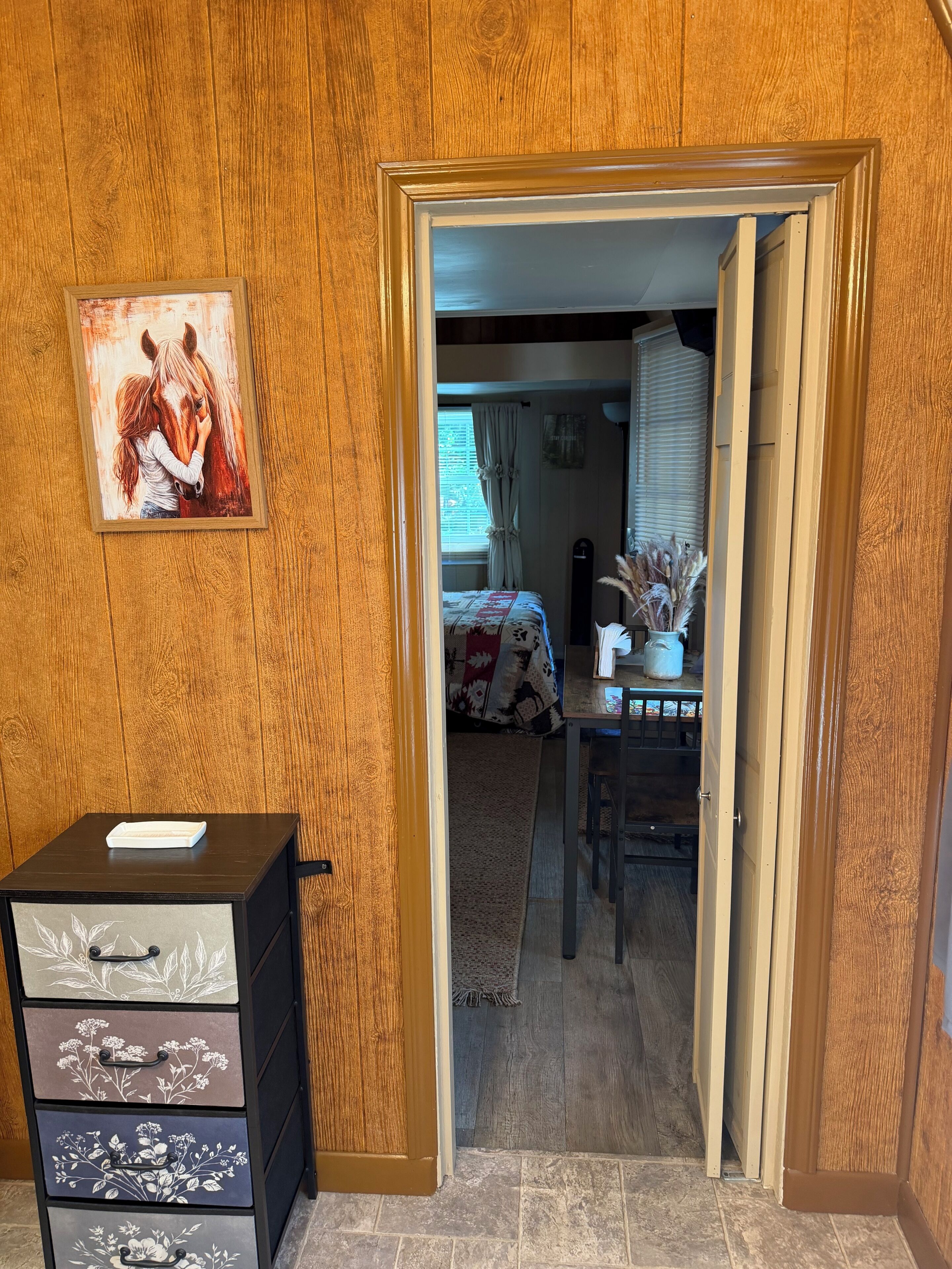 A wooden-paneled room with a bed, a desk, and a framed painting.