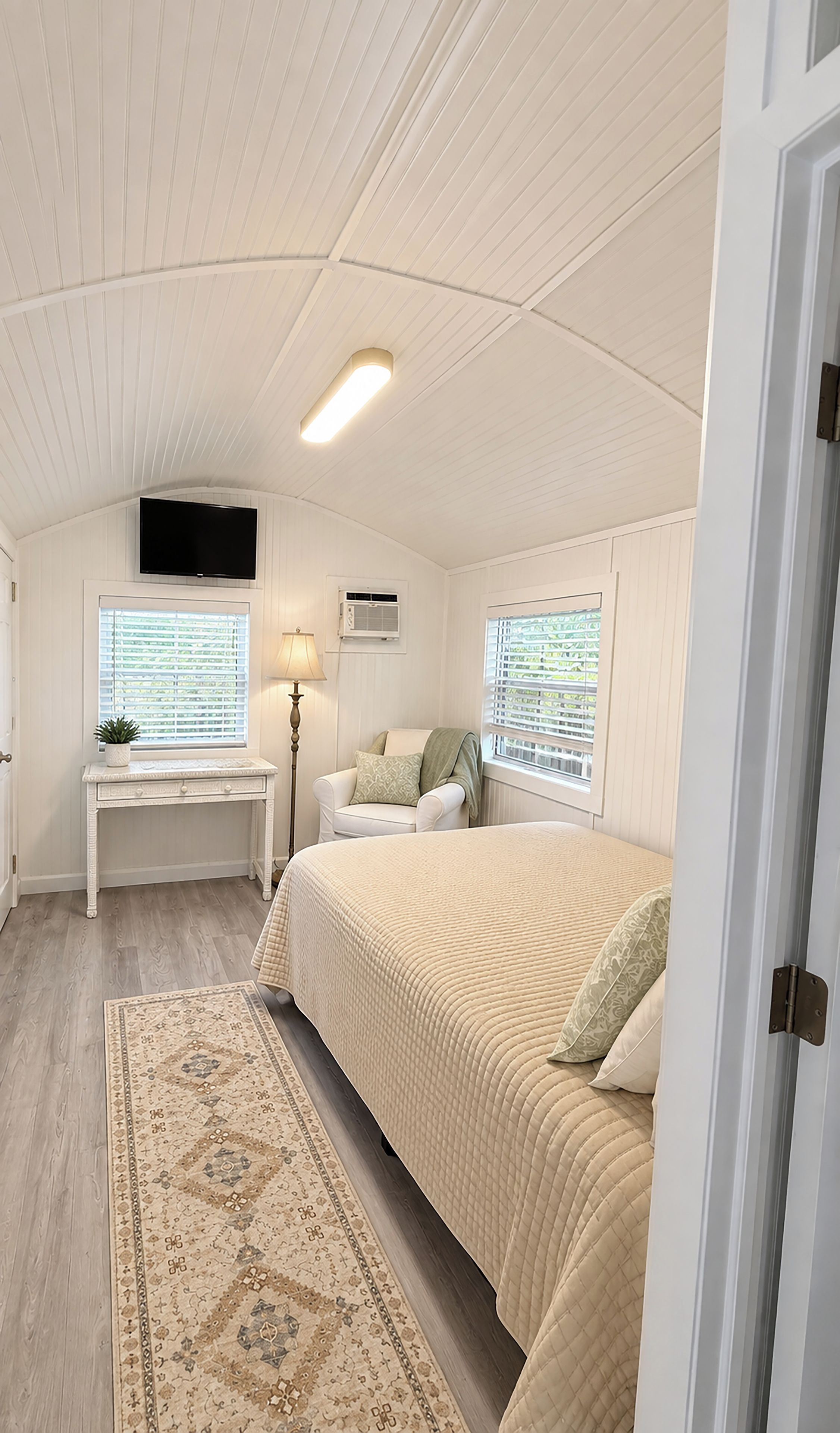 A bedroom with a bed, a desk, a TV, and a window with blinds.