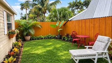 Ein Garten mit Holzzaun, Rasenfläche, einem weißen Stuhl und roten Stühlen.