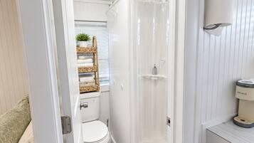 A compact bathroom with a toilet, a shower enclosure, and a built-in coffee maker.