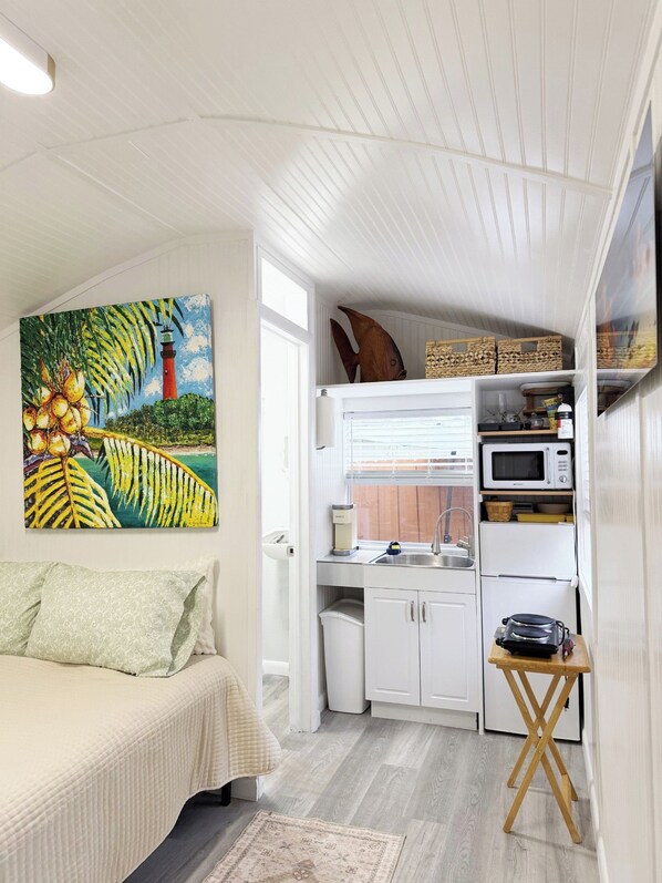 A compact living space with a bed, a kitchenette, and a painting on the wall.