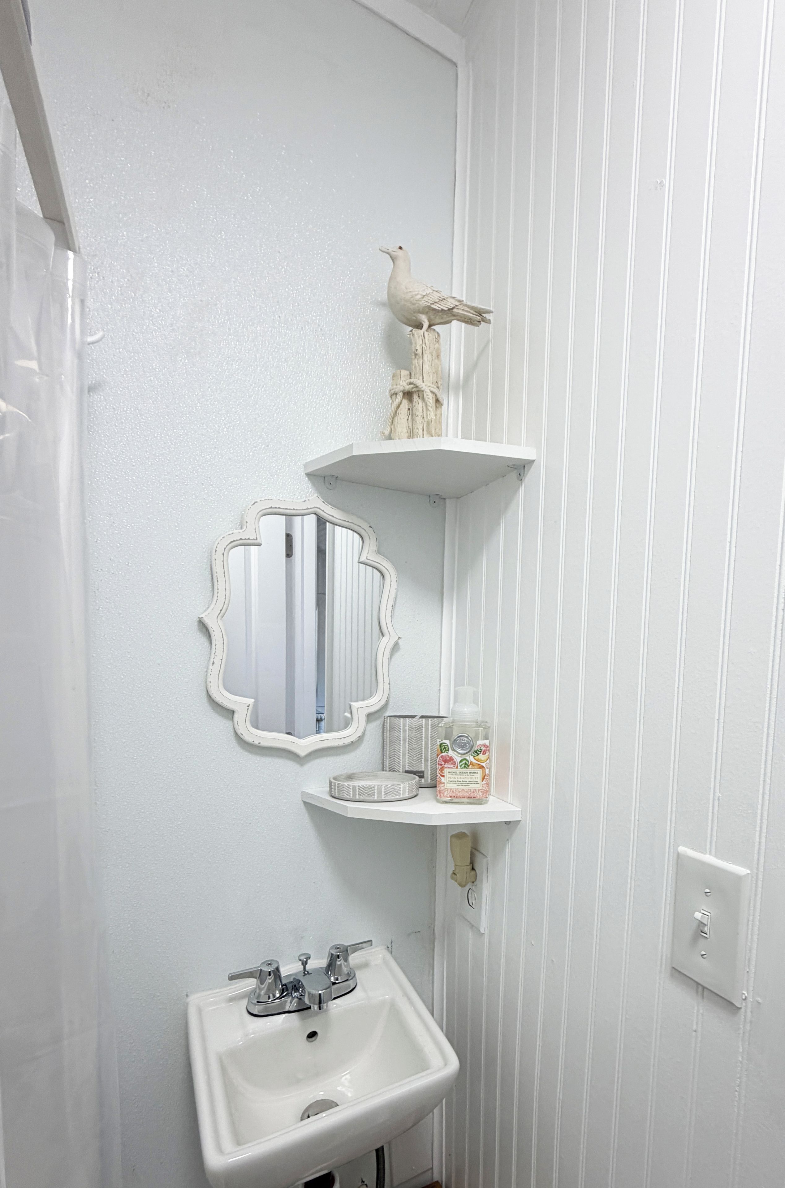 A bathroom with a white sink, a mirror, and two shelves with toiletries.