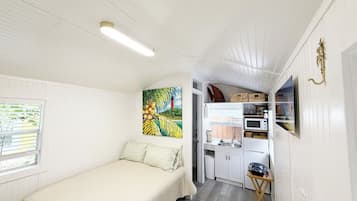 A compact room with a bed, a painting, a kitchenette, and a small window.