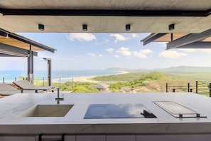 A modern kitchen with a large countertop and a view of the ocean and hills. - Hottub w/Elite Ocean View! | Chef`s Kitchen | 3 Pools | Personal Concierge (Tamarindo)