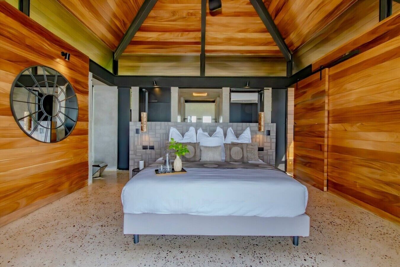 A modern bedroom with a large bed, a circular mirror, and a unique ceiling design.