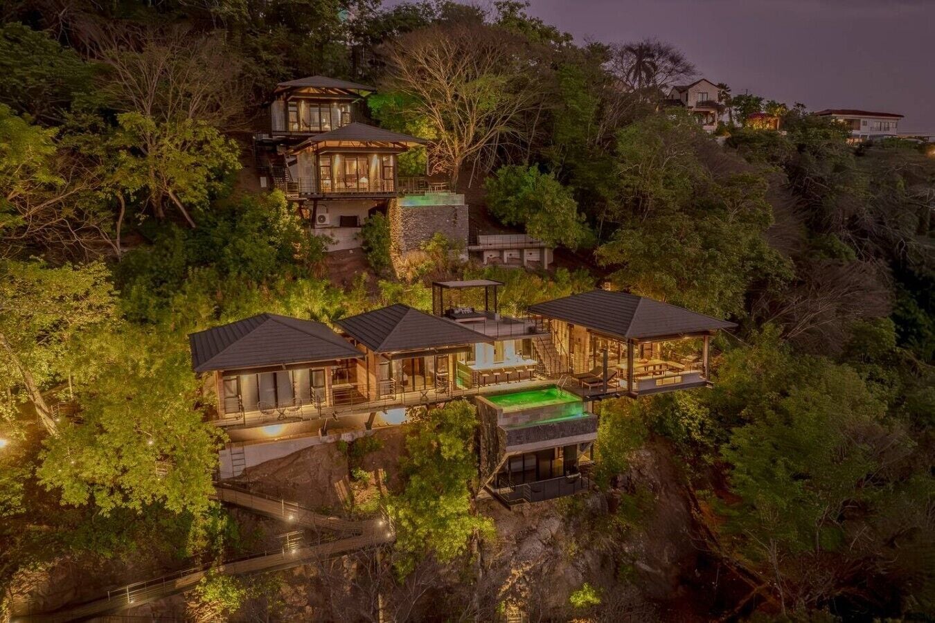 A multi-story residential property with a pool, surrounded by dense vegetation.