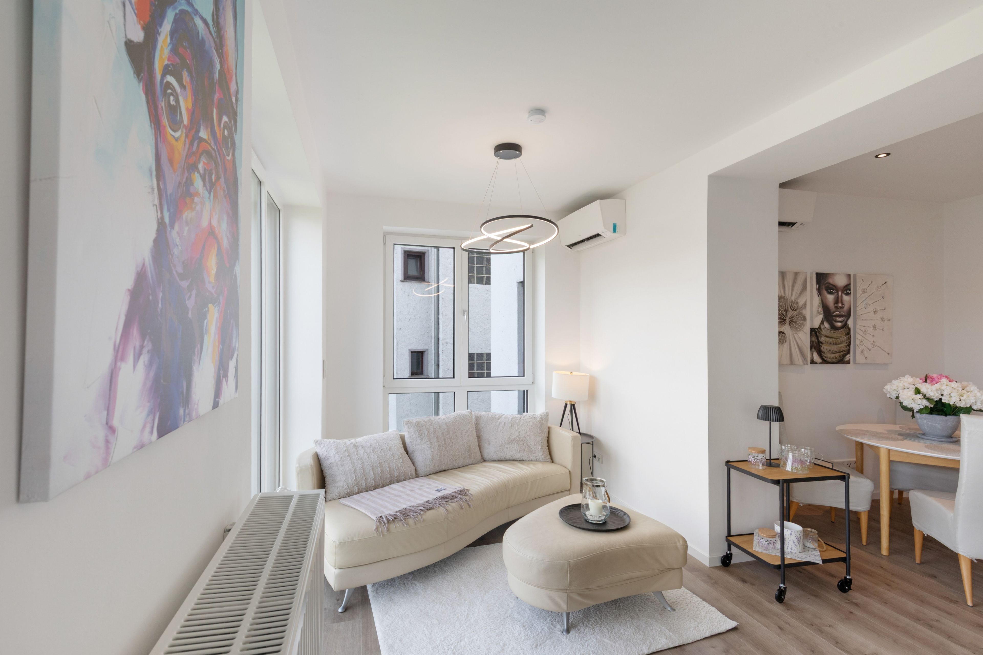 A modern living room with a sofa, ottoman, and a dining area with a table and chairs.