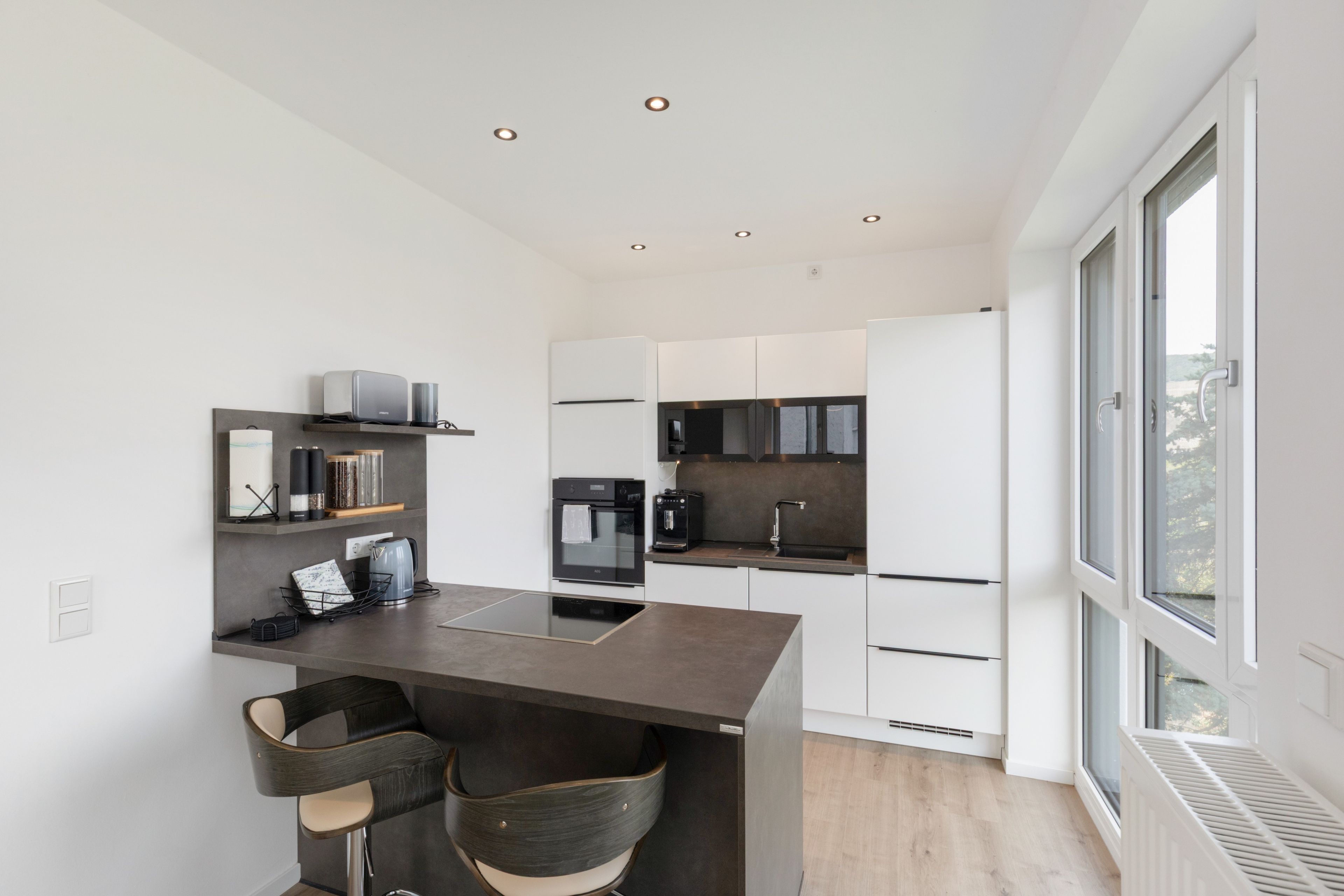 A modern kitchen with a central island, built-in appliances, and a large window providing natural light.