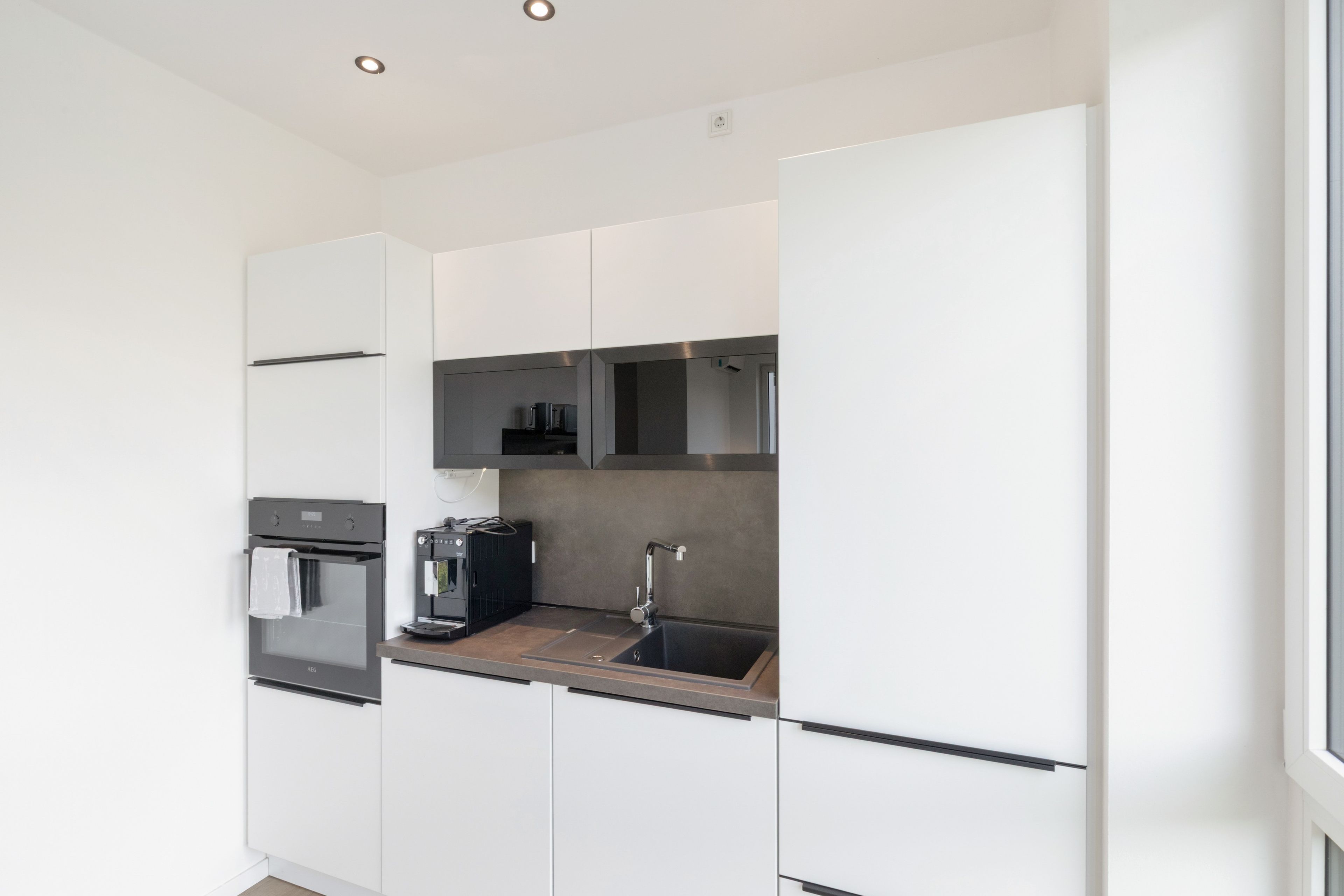 Eine moderne Küche mit weißen Schränken, einem Backofen, einer Kaffeemaschine und einem Spülbecken.