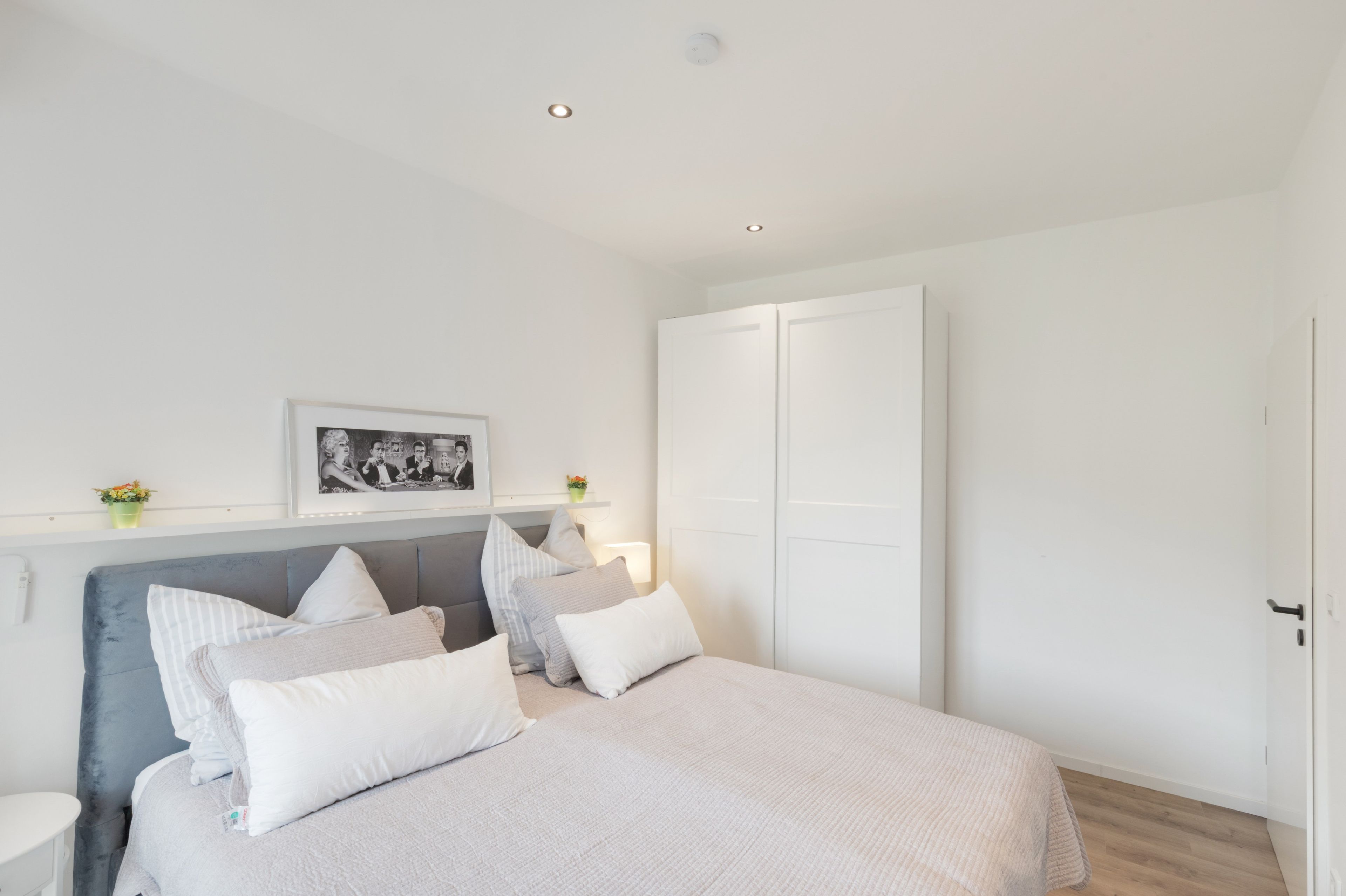 A bedroom with a bed, bedside tables, a nightstand, a framed picture, a wardrobe, and a ceiling light.