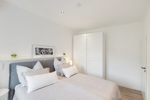A bedroom with a bed, bedside tables, a nightstand, a framed picture, a wardrobe, and a ceiling light. - Apartment 'EG Whg mit Aussicht Nahe, Burg Klopp, Niederwald, 55" TV & WLAN & Klimaanlage' (Bingen)