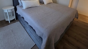 Ein modernes Schlafzimmer mit Bett, Nachttischen, einem Schrank und einem Wandregal mit Pflanzen.