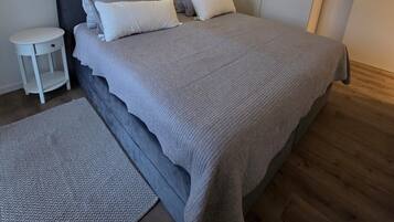 Ein modernes Schlafzimmer mit Bett, Nachttischen, einem Schrank und einem Wandregal mit Pflanzen.