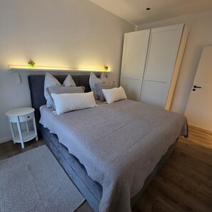 Een moderne slaapkamer met een bed, nachtkastjes, een kledingkast en een wandplank met planten.