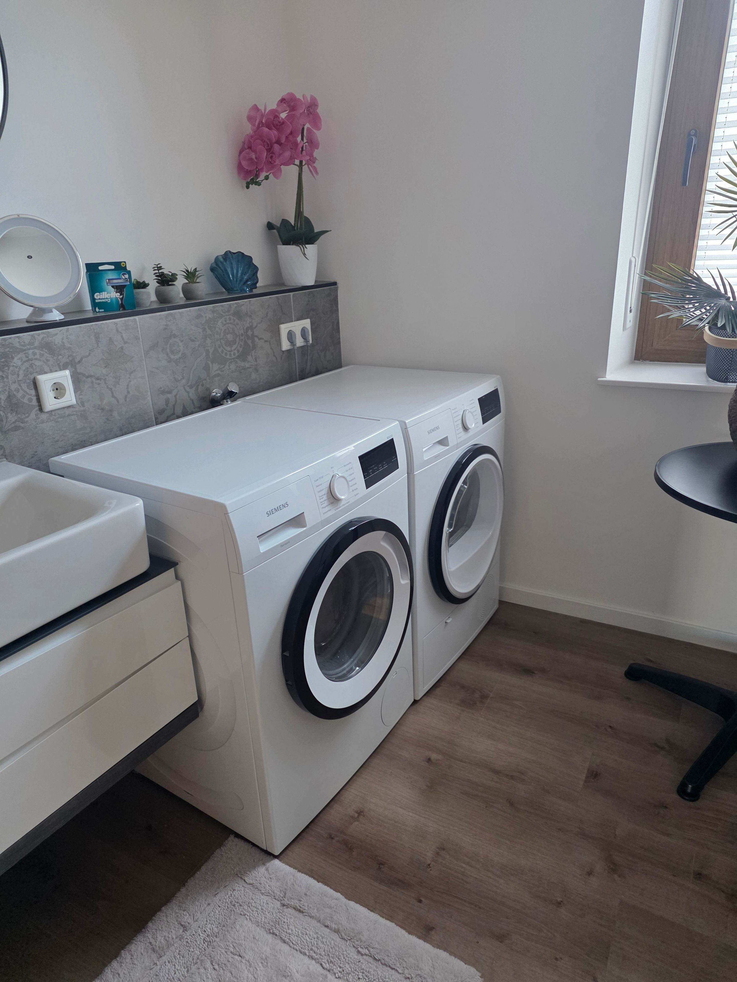 A compact laundry area with a washing machine and dryer, a sink, and a small window with a plant.