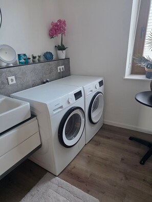 A compact laundry area with a washing machine and dryer, a sink, and a small window with a plant. - Apartment 'EG Whg mit Aussicht Nahe, Burg Klopp, Niederwald, 55" TV & WLAN & Klimaanlage' (Bingen)