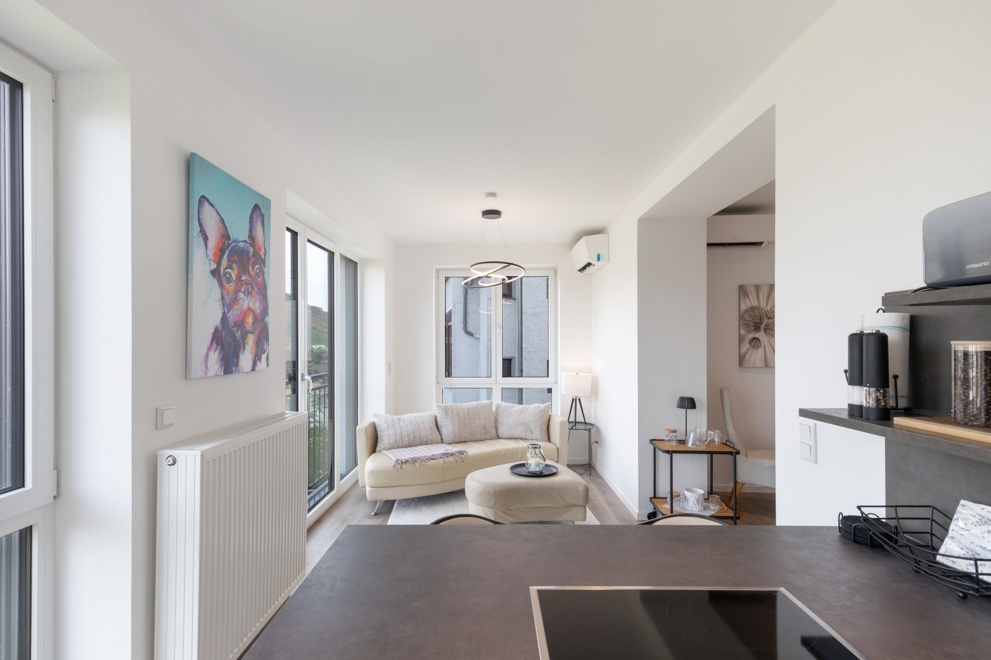 Eine moderne Küche mit einer Kochinsel, einer Essecke mit einer Couch und einem großen Fenster mit Blick ins Freie.