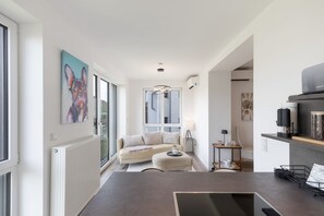 A modern kitchen with a central island, a dining area with a sofa, and a large window providing a view of the outdoors.