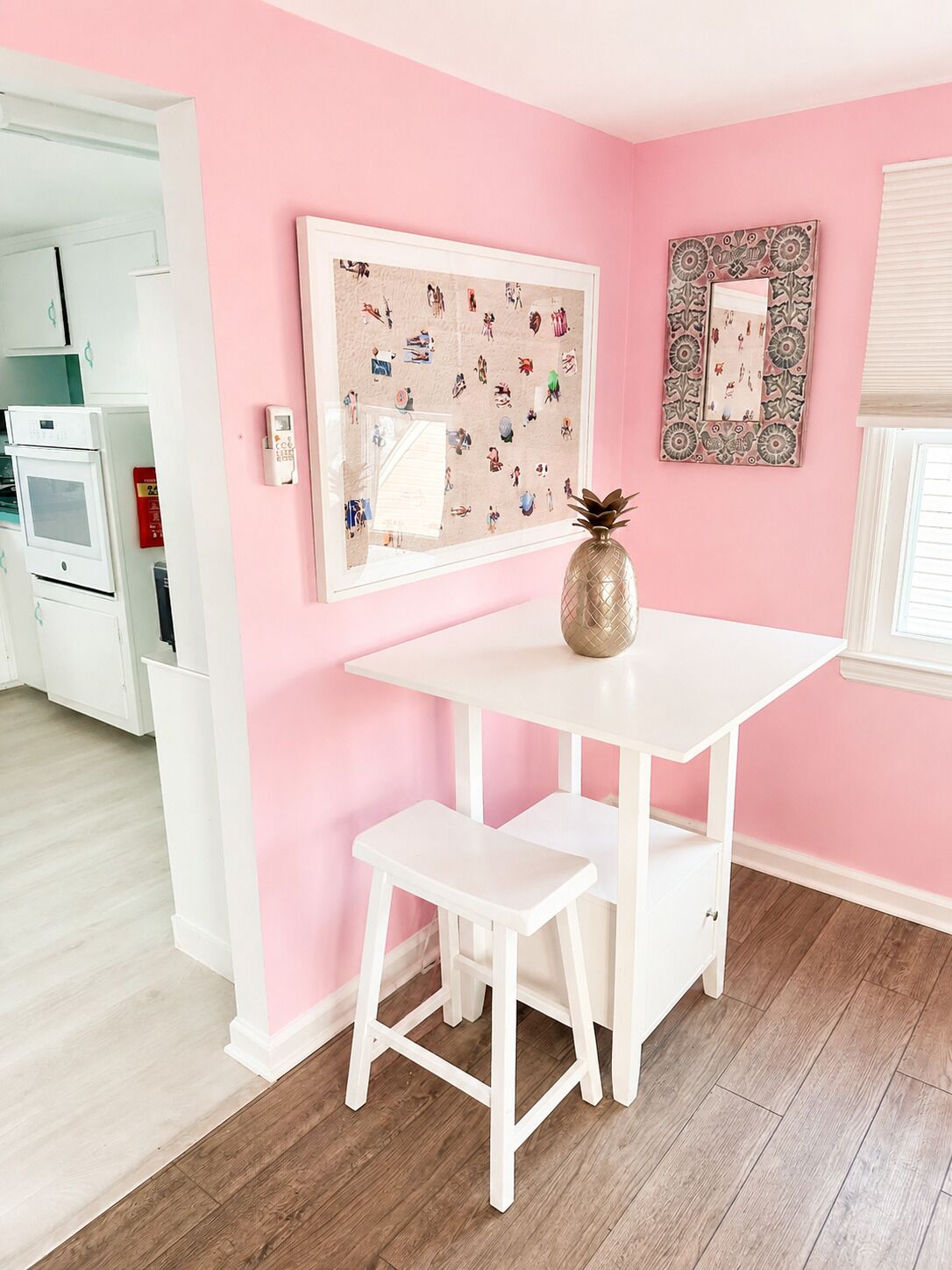 A room with a white table and bench, pink walls, a decorative mirror, and a framed picture.