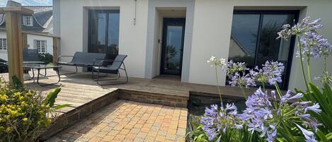 Una casa moderna con patio, mobiliario exterior y jardín lleno de flores.