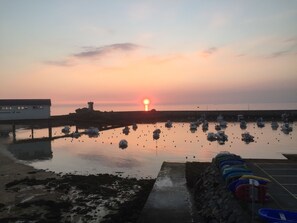 Ein Sonnenuntergang über einem ruhigen Hafen mit Booten, einer Pier und einem Gebäude mit Beschilderung.