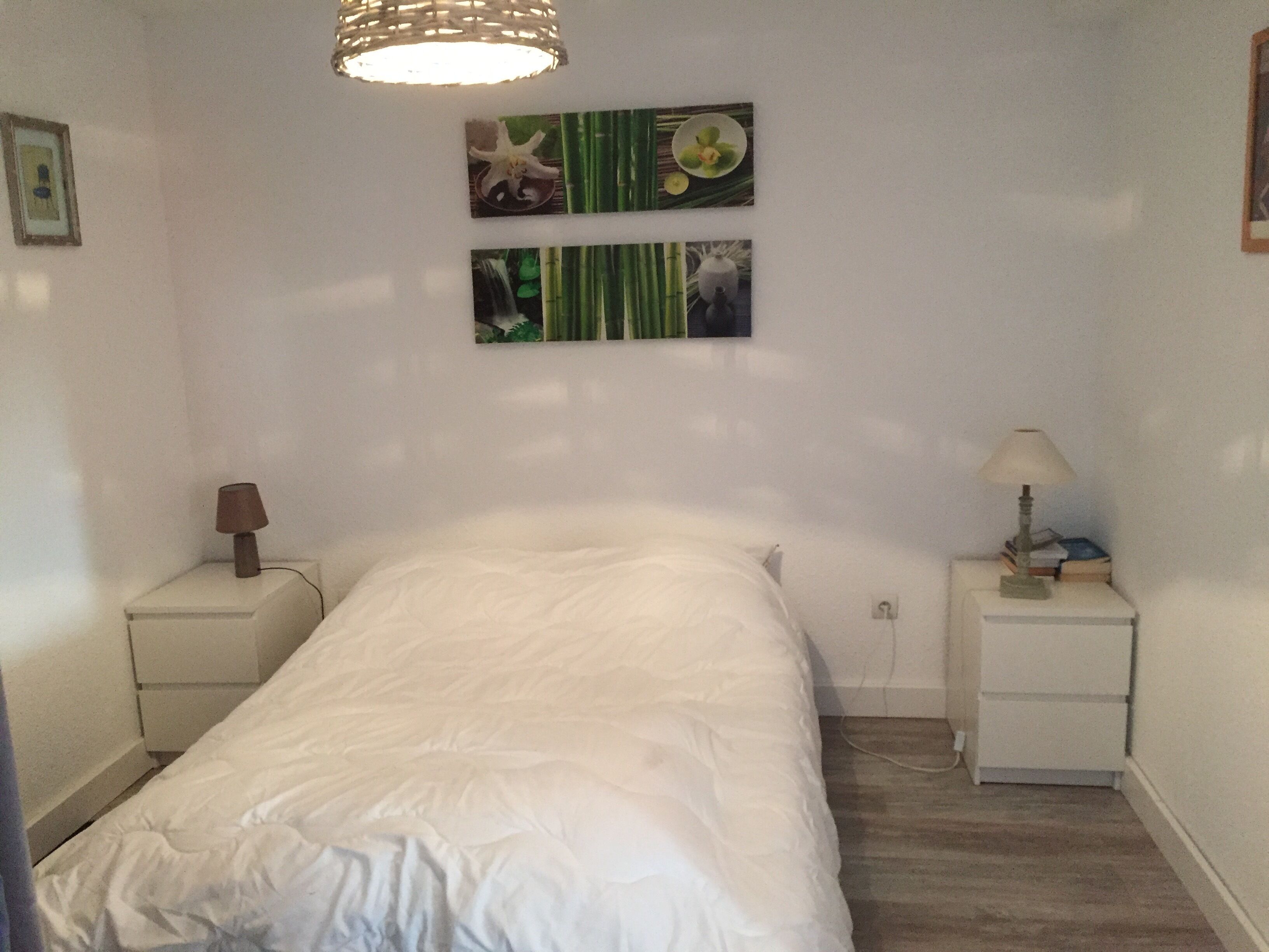 A bedroom with a bed, two bedside tables, a lamp, and wall art.
