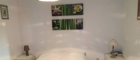 A bedroom with a bed, two bedside tables, a lamp, and wall art.