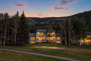 Une maison à deux étages avec un balcon, entourée d’arbres et située dans un paysage vallonné.