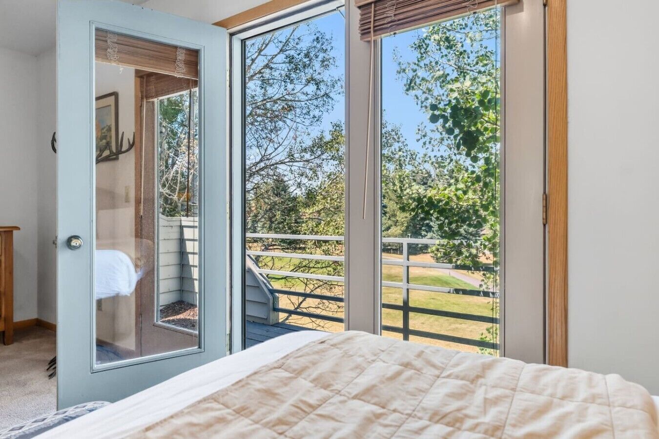 A bedroom with a bed, a door leading to a balcony, and a view of trees and grass.