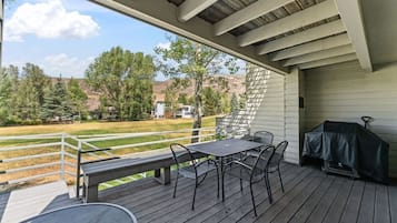 En overdækket terrasse med et bord og stole, grill og udsigt til græsplæne og træer.