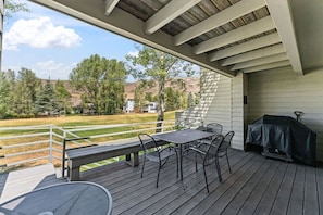 A covered outdoor patio with a table and chairs, a grill, and a view of a grassy yard and trees. - Golf Course Views W/ EagleVail Amenities (avon)